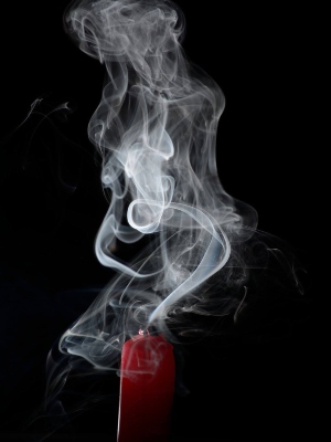An extinguished red candle puts off white smoke against a black background.