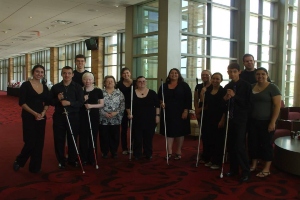 A group dressed in all black holding white canes poses for the camera.
