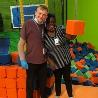 A young male and female smile and pose for the camera in front of a pile of multicolored foam blocks. 