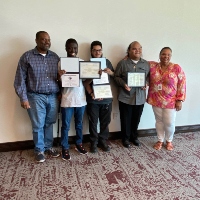 A man and woman pose along side three young men smiling and hold certificates and diplomas. 